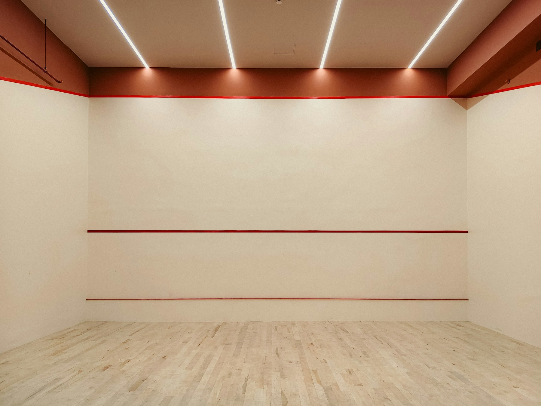 An empty squash court with red front-wall lines and a timber floor.